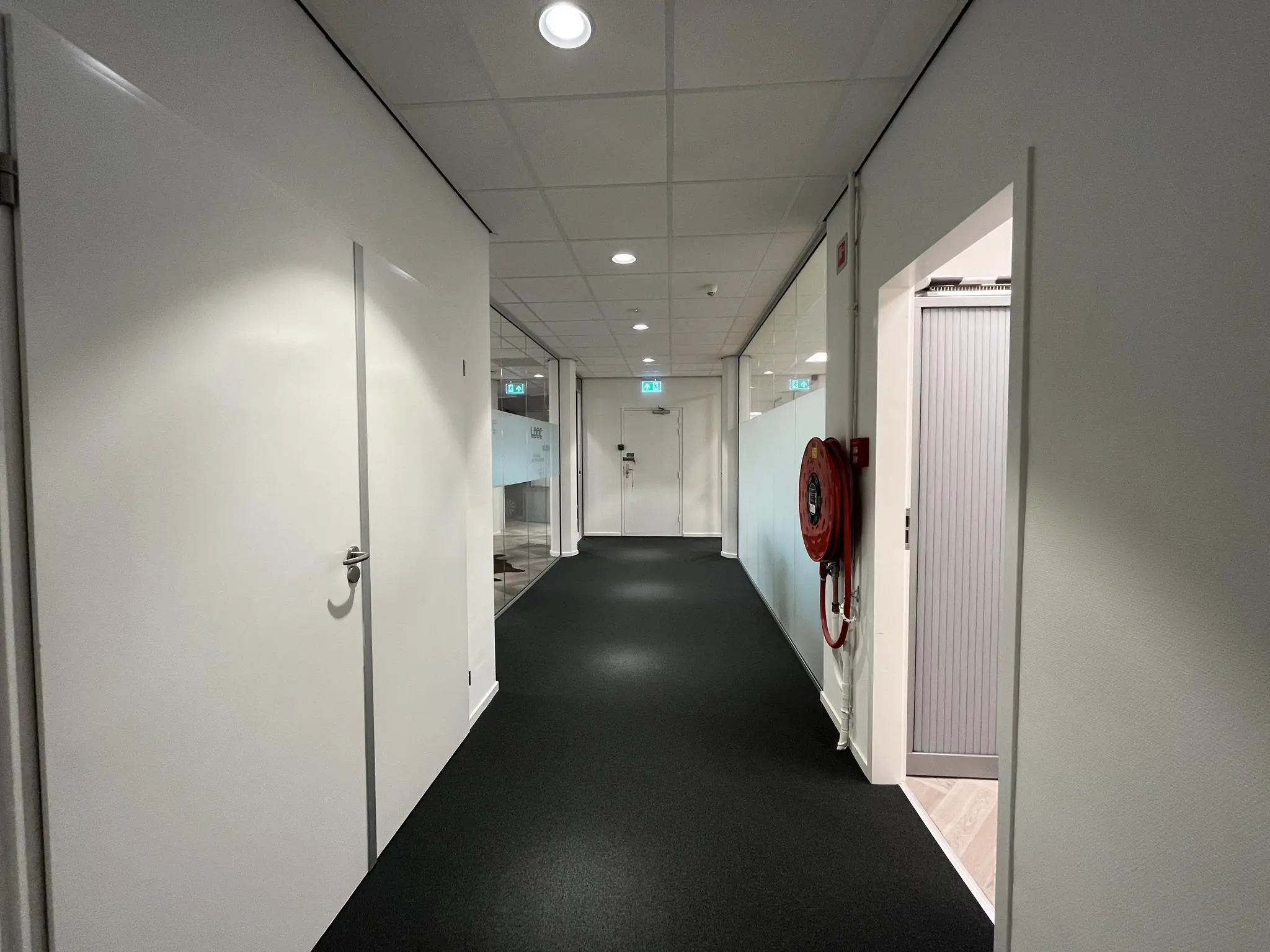 Binnenhal van een kantoorpand aan de Lange Dreef met witte deuren, glazen wand, brandslanghaspel en zwart tapijt.